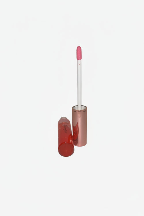 Pink lip gloss with a white applicator on a light surface